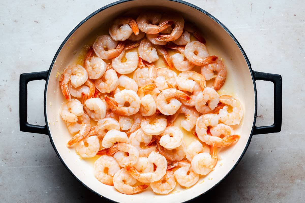 A large round pot filled with cooked shrimp in a light sauce, viewed from above on a neutral-colored surface.