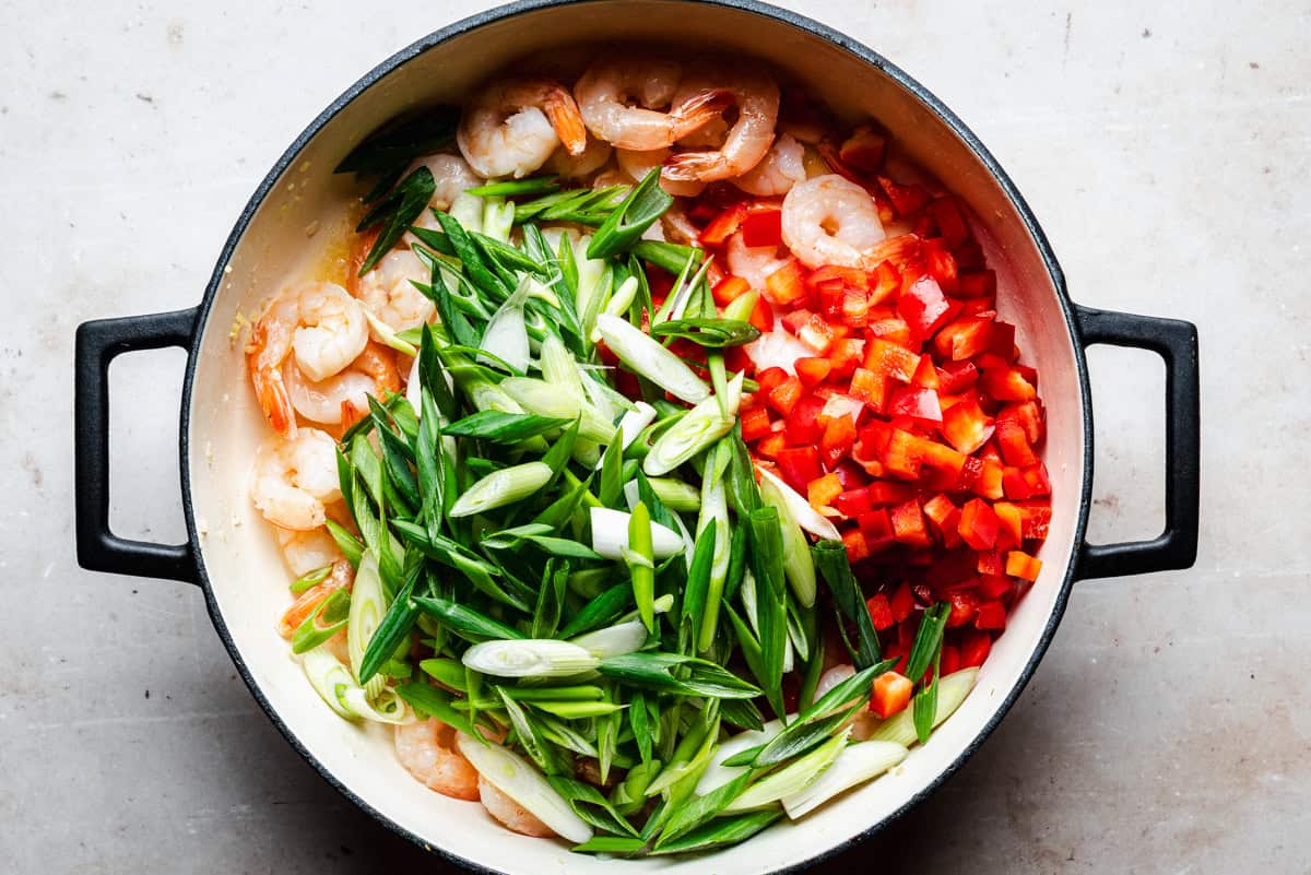 A large pot filled with shrimp, sliced green onions, and diced red bell peppers, all arranged in separate sections, ready to be cooked.