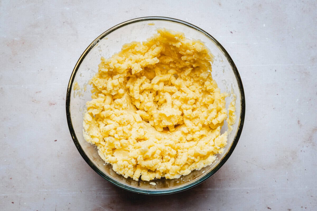 A glass bowl filled with freshly mashed potatoes sits on a light-colored countertop. The mashed potatoes appear creamy with a slightly lumpy texture.