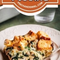 A slice of savory bread pudding with spinach and cheese sits on a white plate with a fork. Another plate and a glass of water are in the background. A sign above reads "Savory Bread Pudding" from pinchandswirl.com.