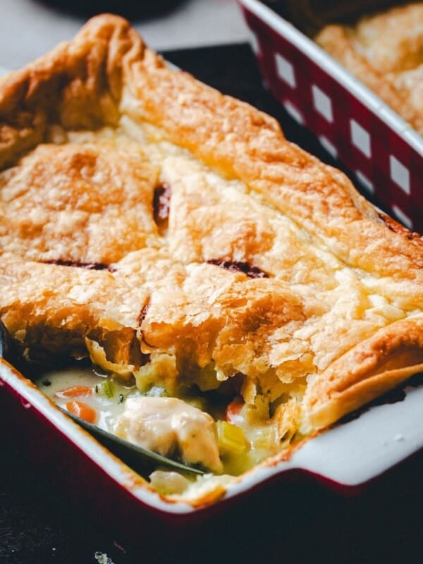 Golden, flaky puff pastry tops a rectangular baking dish filled with creamy turkey pot pie, visible chunks of turkey, carrots, and celery; a serving spoon rests inside the dish.