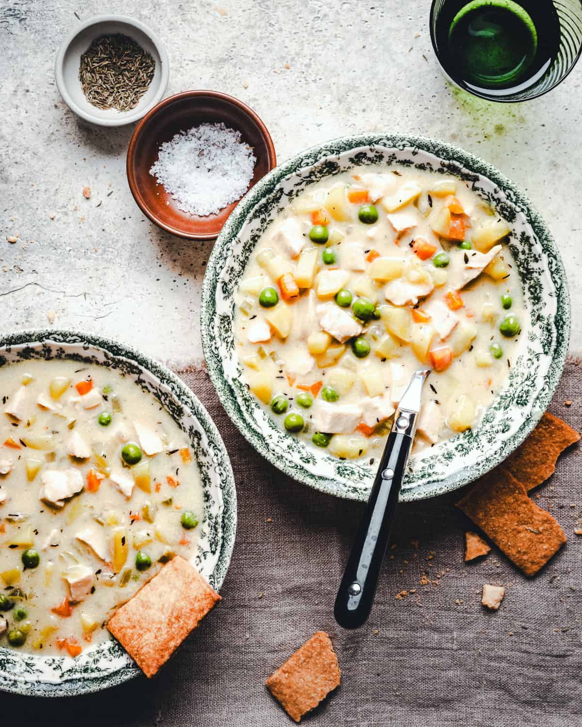 Two bowls of soup with a spoon and crackers.