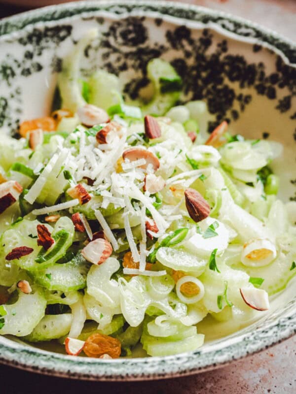 A bowl with a green and white floral pattern filled with a salad of sliced celery, green onions, chopped almonds, and shredded cheese, garnished with fresh herbs.