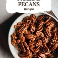 A bowl filled with crispy, glazed praline pecans on a neutral background. Text above the bowl reads: "Crispy, Buttery Praline Pecans Recipe." The words "pinch and swirl" appear in the bottom left corner.