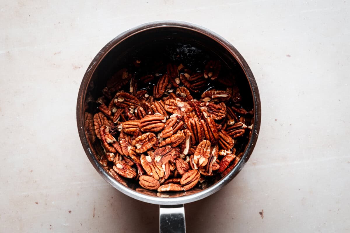 A metal saucepan filled with pecan halves, sitting on a light-colored countertop.