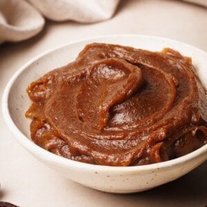 A white bowl filled with smooth, creamy date caramel, with swirled texture on top, set on a light surface.