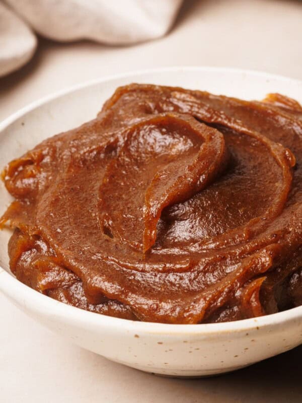 A white bowl filled with smooth, creamy date caramel, with swirled texture on top, set on a light surface.