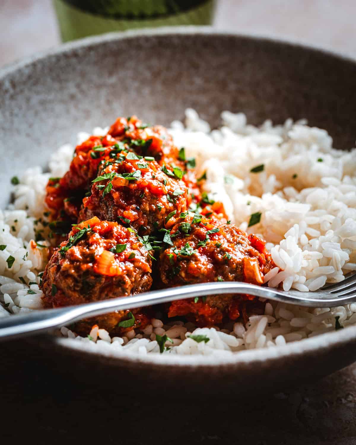 A bowl of white rice topped with several Mexican meatballs in chipotle sauce, garnished with chopped herbs. A fork rests on the edge of the bowl.