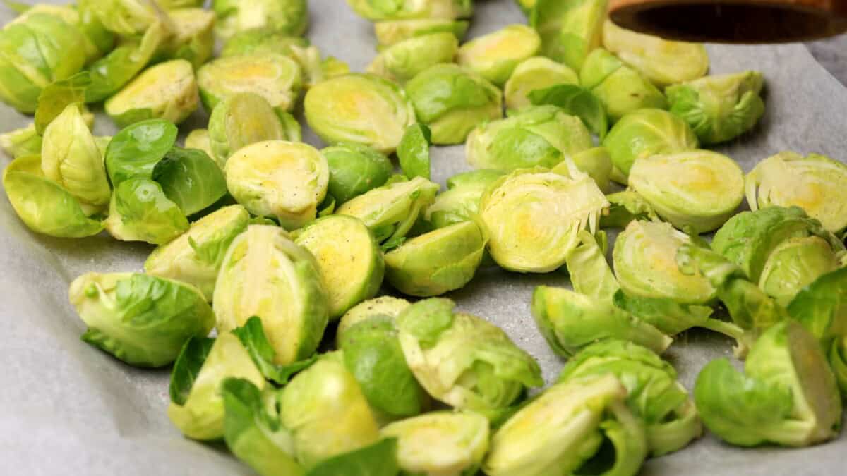 Halved and seasoned Brussels sprouts scattered on a parchment-lined baking sheet, ready for roasting.