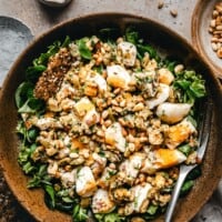 A bowl of Mediterranean egg salad topped with pine nuts and herbs, served on a bed of greens with seed crackers on the side. Text above reads "Pinch and Swirl Mediterranean Egg Salad.