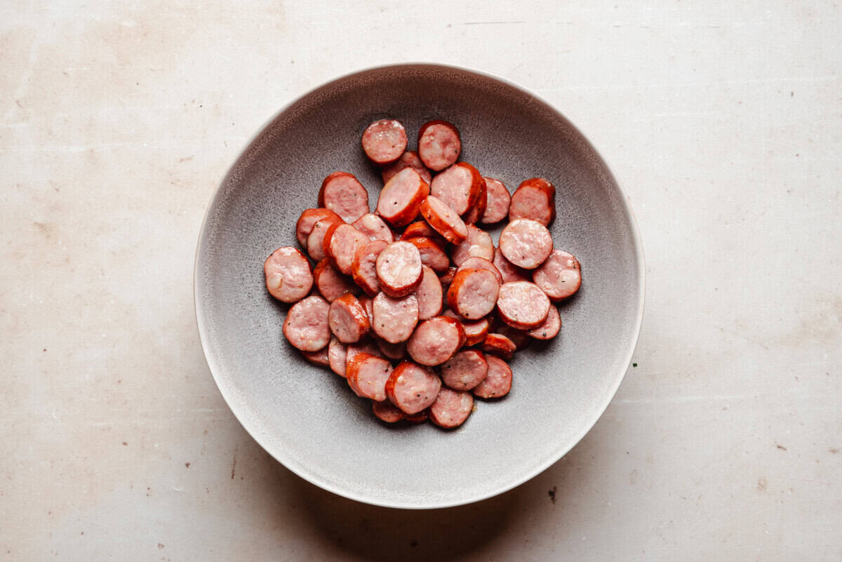 A gray bowl filled with sliced cooked sausage pieces sits on a light-colored, speckled countertop.