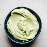 A blue bowl filled with creamy, light green avocado crema sits on a light-colored surface. Text at the top reads "Pinch and Swirl Avocado Crema" and the website "pinchandswirl.com" is at the bottom.