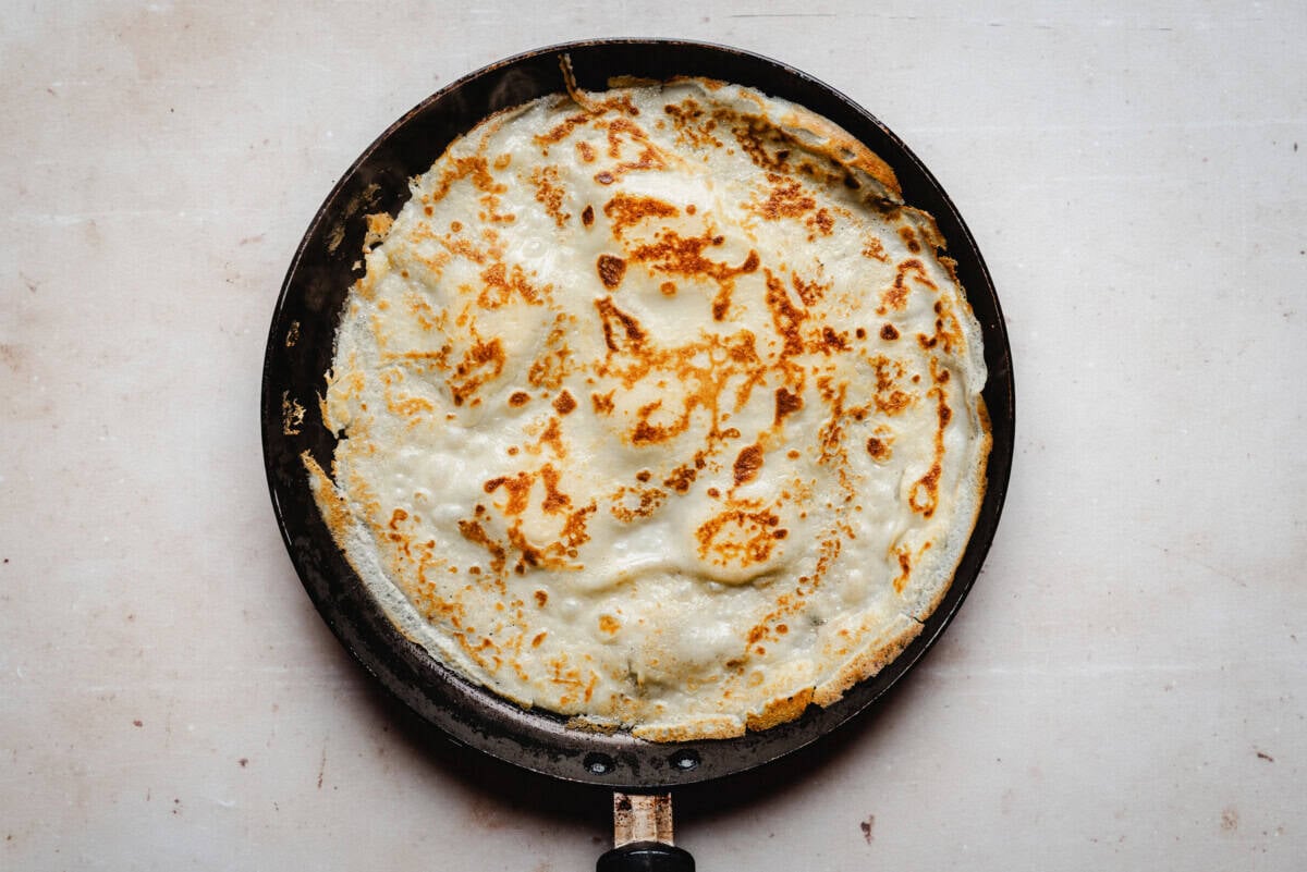Banana crepe with golden-brown, crispy edges cooking in a black frying pan.