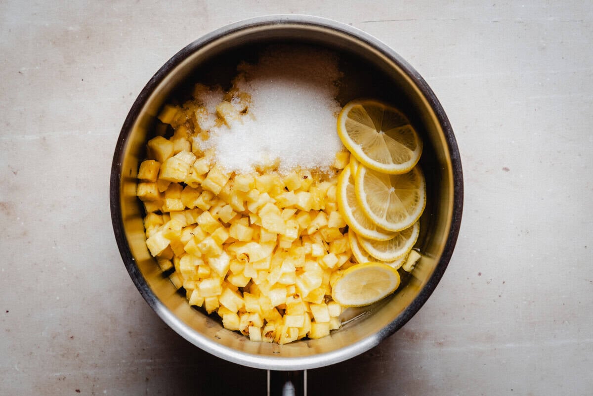 Saucepan with diced pineapple and lemon slices for pineapple marmalade, ingredients separated on the pan bottom.
