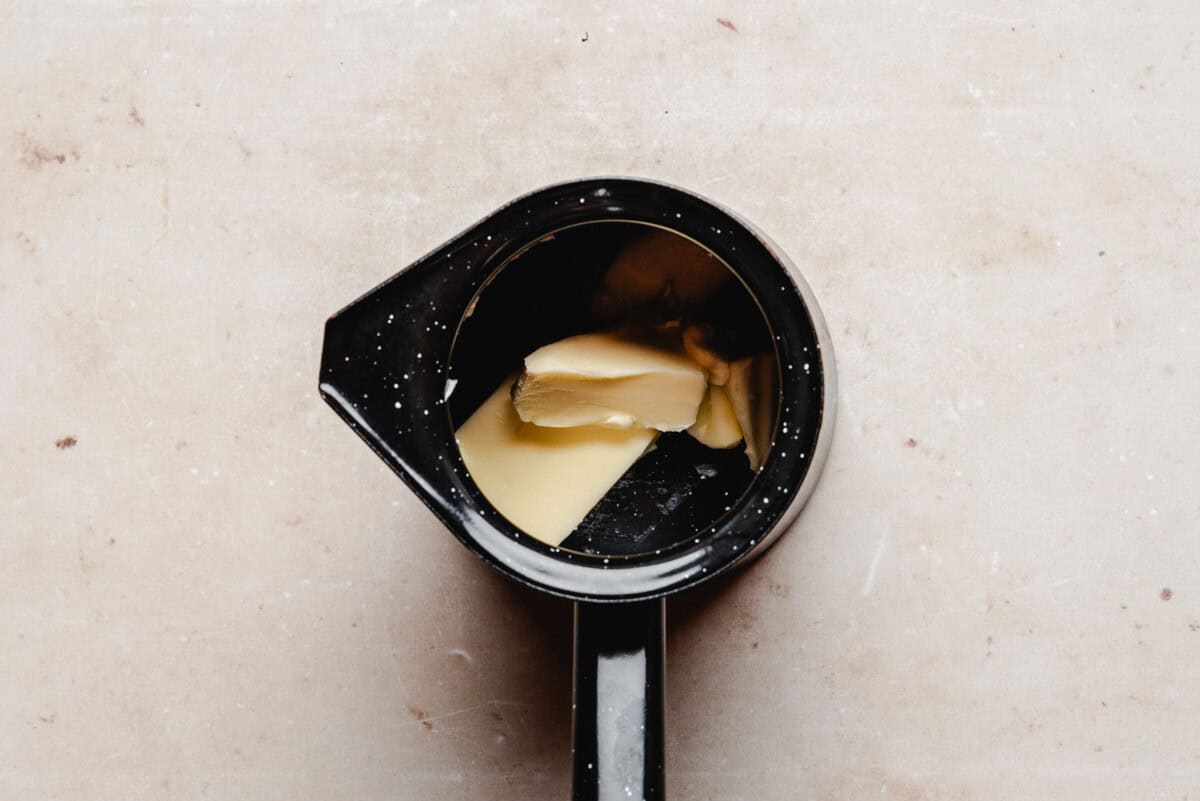 A black saucepan with chunks of butter, viewed from above on a light surface.
