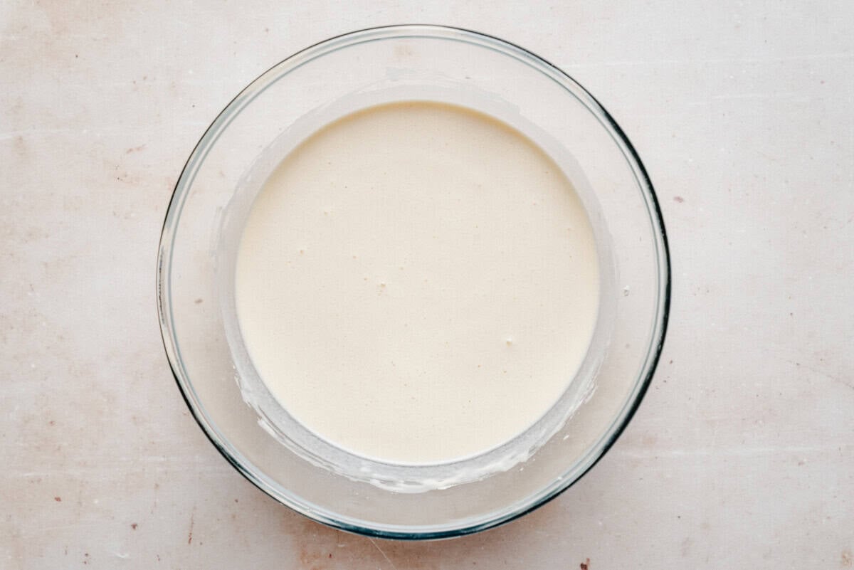 Crepe batter in a glass bowl, showcasing its smooth, pale texture from an overhead view.