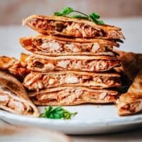A stack of sliced chicken tinga quesadillas with golden, crispy tortillas and shredded chicken filling, garnished with fresh cilantro on a white plate.