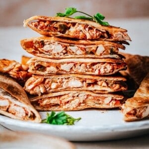 A stack of sliced chicken tinga quesadillas with golden, crispy tortillas and shredded chicken filling, garnished with fresh cilantro on a white plate.