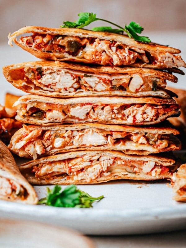 A stack of sliced chicken tinga quesadillas with golden, crispy tortillas and shredded chicken filling, garnished with fresh cilantro on a white plate.