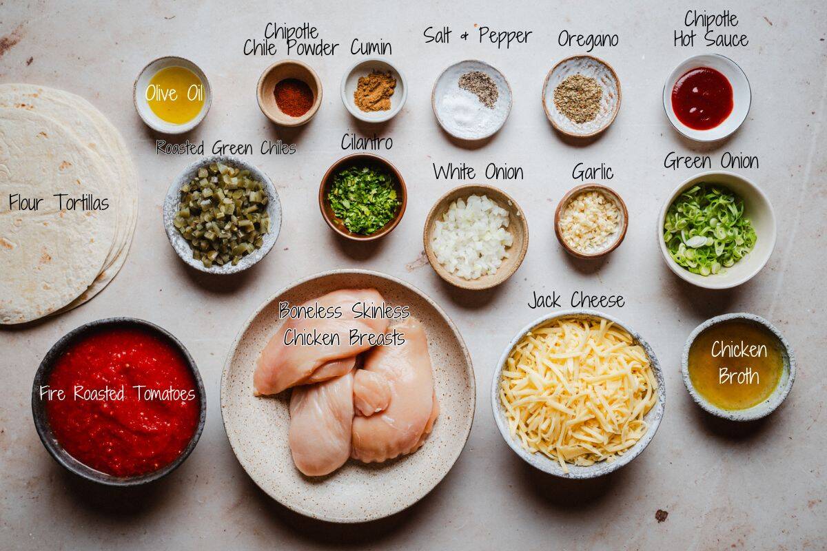 A top view of various labeled ingredients for chicken tinga quesadillas, including tortillas, chicken breasts, shredded cheese, chopped vegetables, spices, broth, olive oil, hot sauce, and roasted tomatoes arranged on a light surface.