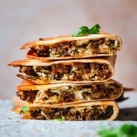 A stack of chorizo quesadillas cut in halves, showing melted cheese, chorizo, and herbs inside golden, crispy tortillas. Garnished with fresh cilantro and set against a blurred background.