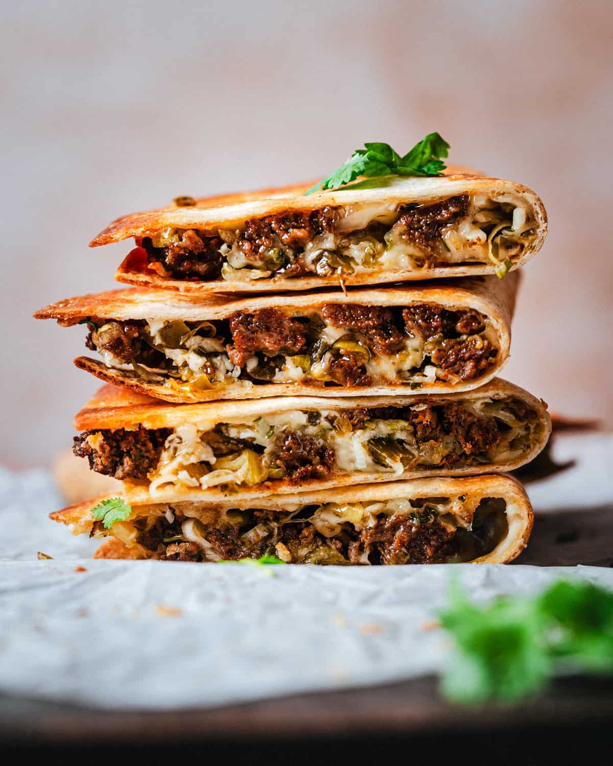 A stack of four crispy chorizo quesadillas halves filled with seasoned ground chorizo, melted cheese, and vegetables, garnished with fresh cilantro on a rustic surface.