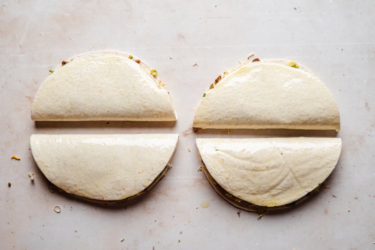 Four folded tortillas are placed side by side on a light-colored surface. The tortillas have a filling inside.