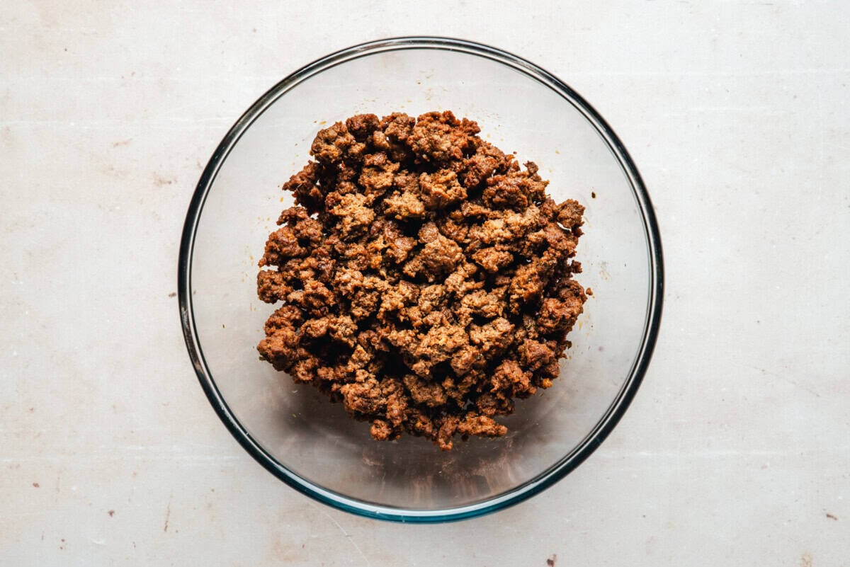 A clear glass bowl filled with cooked, crumbled chorizo sits on a light-colored countertop.