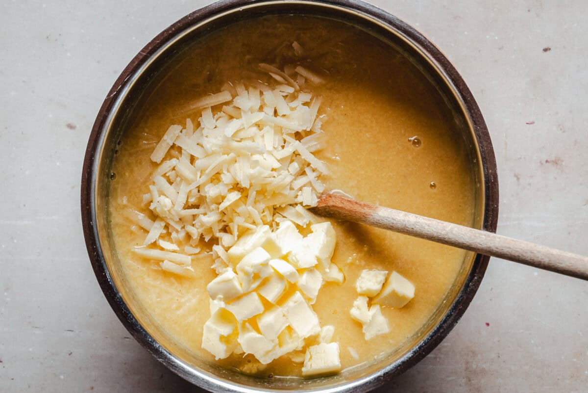 A pot with grated cheese and cubed butter on top of pastina, with a wooden spoon resting inside.