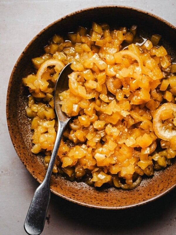 A brown bowl filled with pineapple marmalade with a silver spoon resting inside, placed on a light-colored surface.