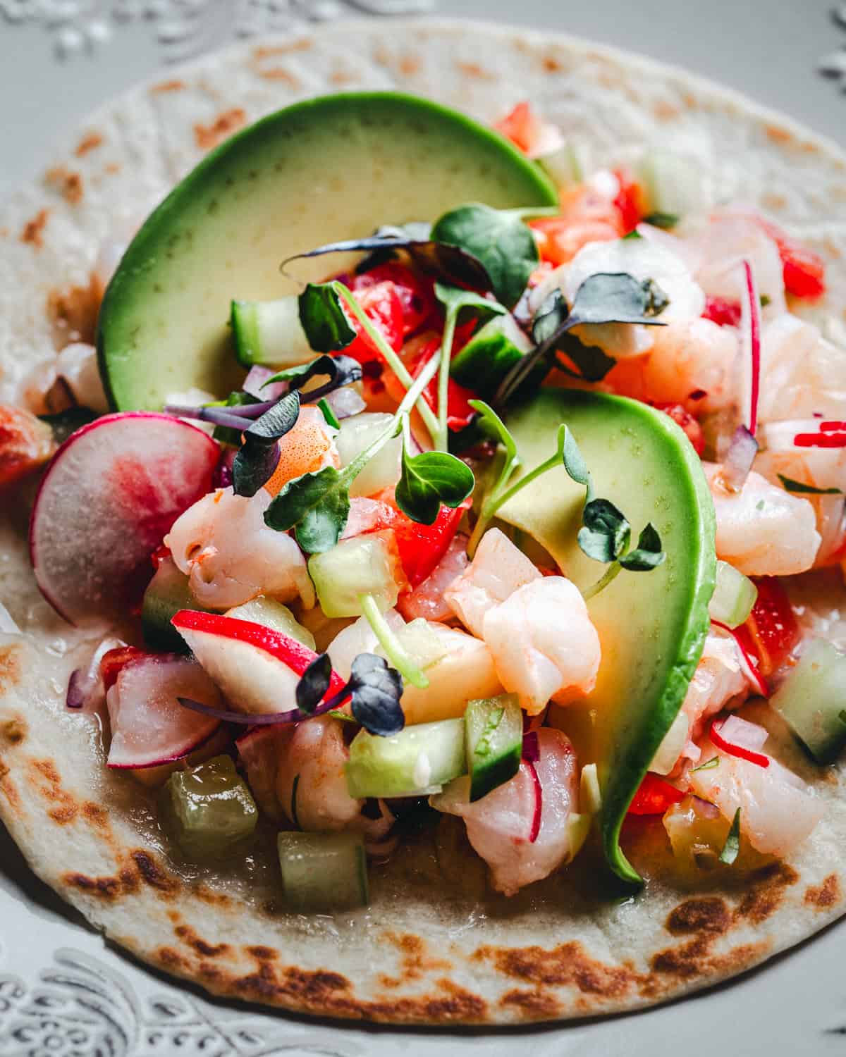 Shrimp ceviche tostada with diced shrimp, cucumber, radish, microgreens, avocado on a soft tortilla.