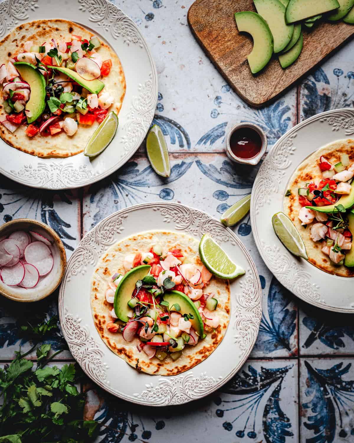 Shrimp ceviche tostada with avocado, tomatoes, onions, cilantro, and lime wedges on corn tortillas.