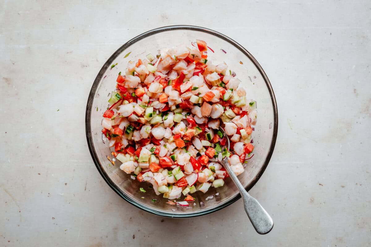 Ceviche with diced shrimp, tomatoes, cucumber, onion, and herbs in a glass bowl.