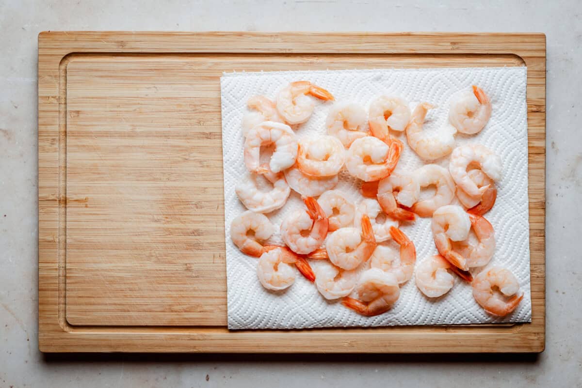 Cooked shrimp arranged on a white paper towel on a wooden cutting board, ready for preparation or serving.