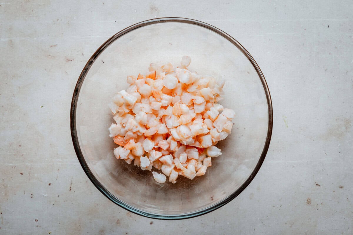 A glass bowl filled with small, diced pieces of shrimp sits on a light-colored countertop.