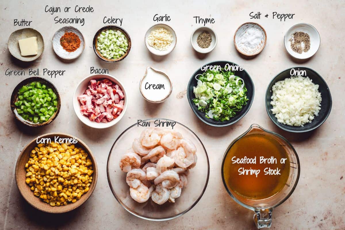 A top-down view of various labeled ingredients in bowls and dishes for shrimp and corn bisque, including shrimp, cream, bacon, corn, chopped vegetables, seasonings, butter, and a measuring cup of seafood broth.