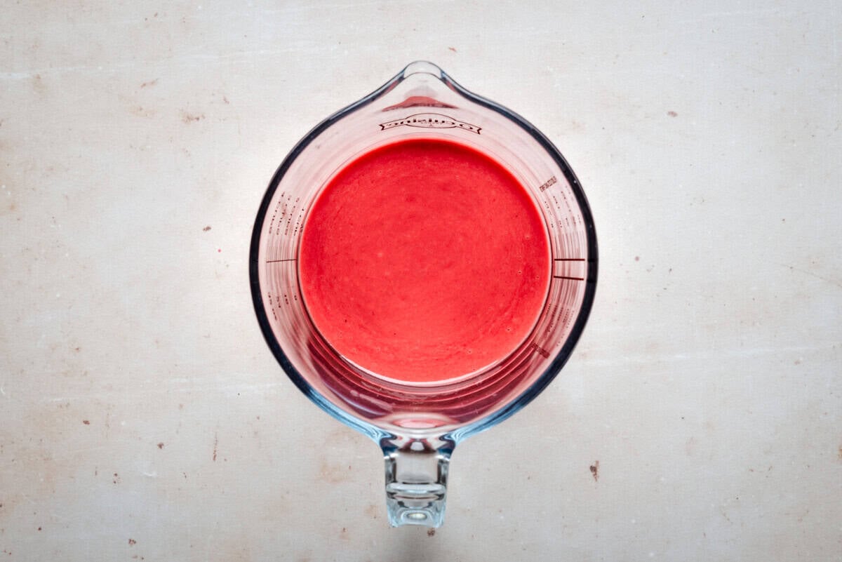 A glass measuring cup filled with a raspberry vinaigrette, viewed from above, sits on a light-colored countertop.