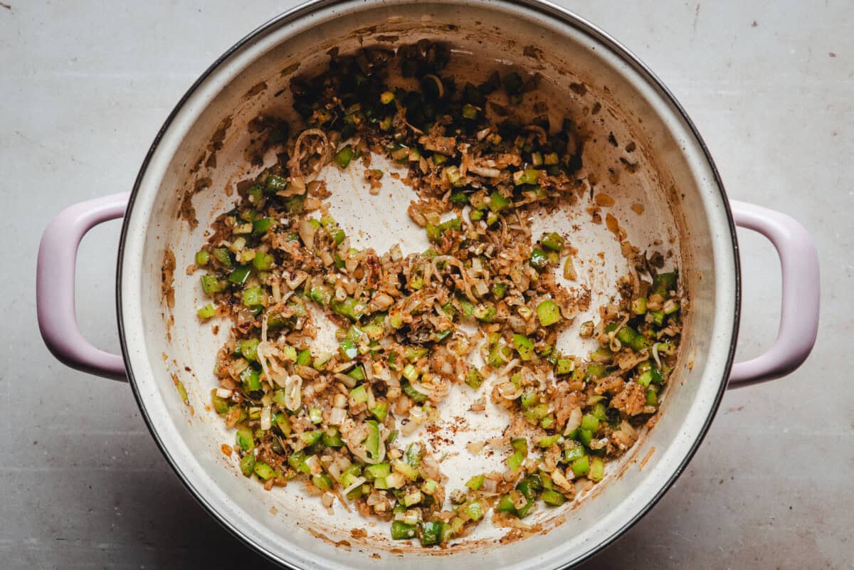 A large pot with chopped onions, green bell peppers, and seasonings sautéing together, with browned bits stuck to the bottom of the pot, indicating the start of a cooked dish.