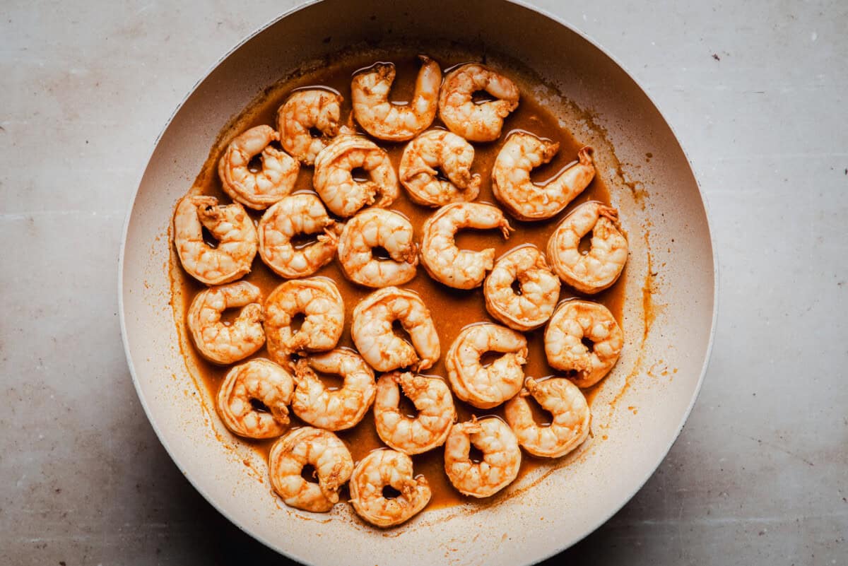 A pan filled with cooked shrimp in a reddish-orange sauce, arranged in a circular pattern on a light-colored surface.